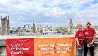 Matt and Tasha wearing matching red Guy's & St Thomas' Charity t-shirts, stood on the roof of St Thomas' Hospital.