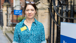 Image of Dr Johanna Feary standing outside of Royal Brompton Hospital's Fulham Wing. She is wearing a green patterned shirt and a yellow name badge on her chest.