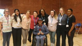 Paralympian and tennis champion, Andy Lapthorne, sitting in a wheelchair with a medal around his chest. He is surrounded by a group of 8 individuals.