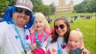 Adrian, Elenie, Stacey and Naia at the British Transplant Games. Adrian is wearing a blue wig, a hat, and an Evelina London Children's Charity t-shirt. Stacey is also wearing a charity t-shirt. Elenie and Naia are wearing pink t-shirts. They are all wearing medals and smiling warmly at the camera. 