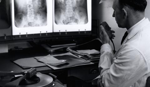 A black and white image of a radiologist looking at X-rays on a light box