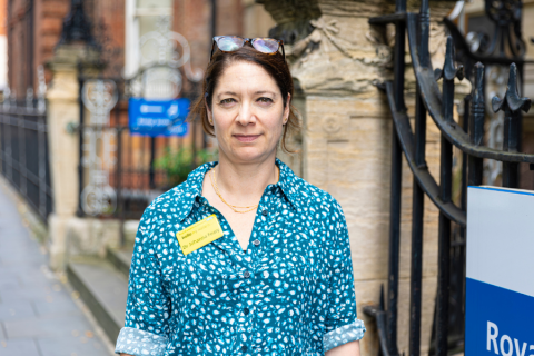 Image of Dr Johanna Feary standing outside of Royal Brompton Hospital's Fulham Wing. She is wearing a green patterned shirt and a yellow name badge on her chest.