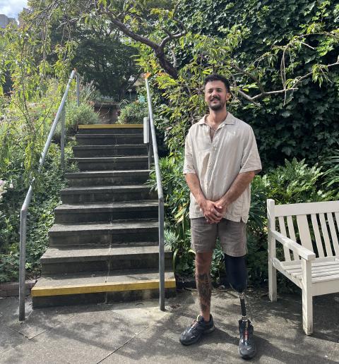 A patient with a prosthesis stands next to steps in a garden