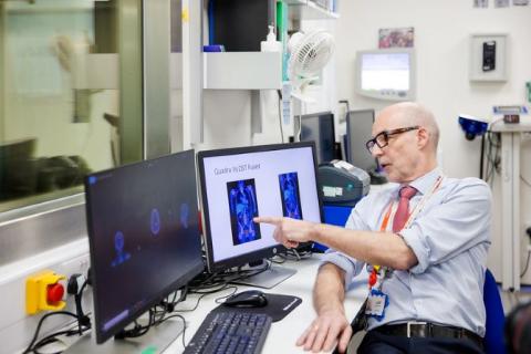 Clinician wearing blue shirt with sleeves rolled up and tie tucked in is pointing to scan images on a computer screen.